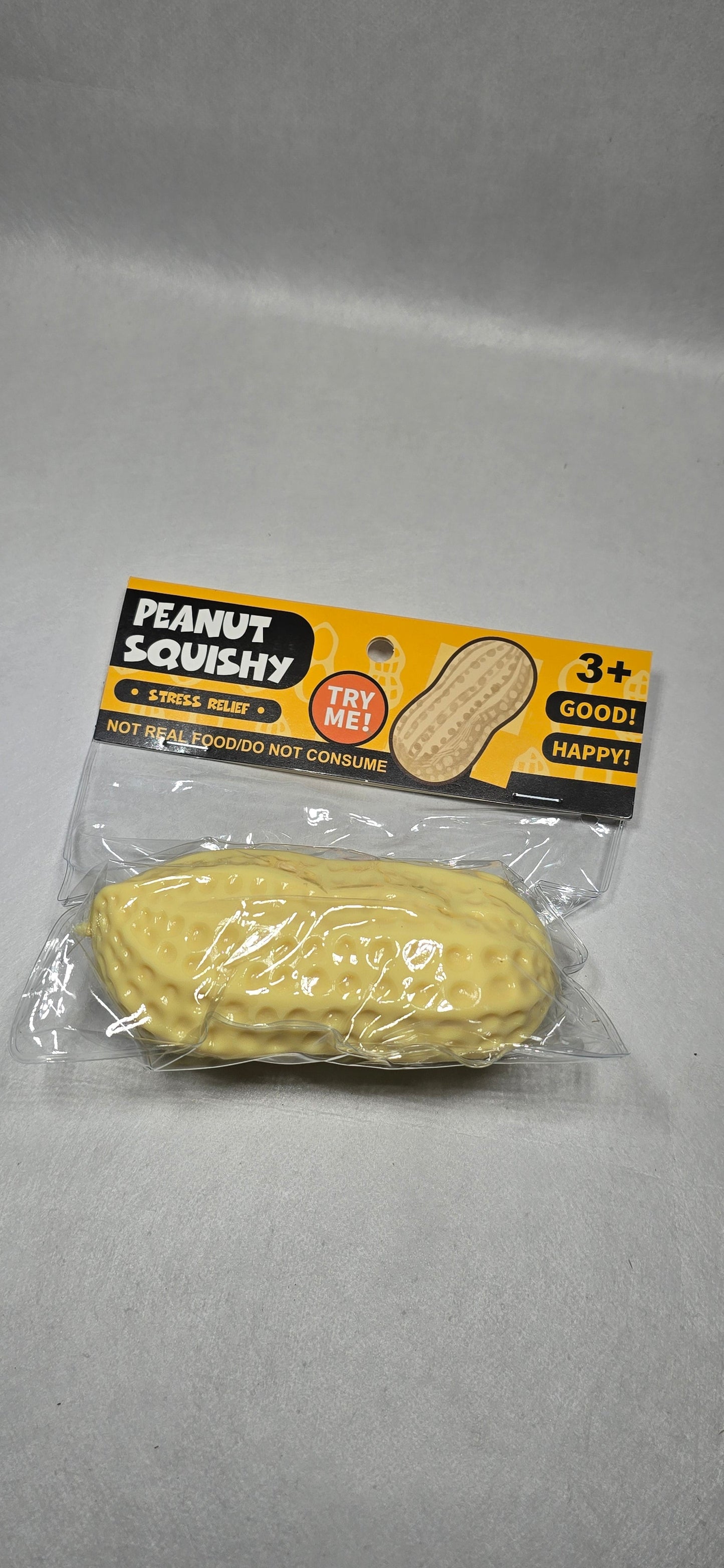 A packaged novelty peanut-shaped squishy toy on a light gray background. The toy is yellow and textured like a peanut, sealed in clear plastic packaging with a yellow and black backing card that reads 'PEANUT SQUISHY'