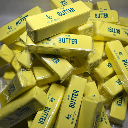 A pile of yellow butter blocks in clear plastic wrappers, with several showing the blue text 'BUTTER' on a gray background.