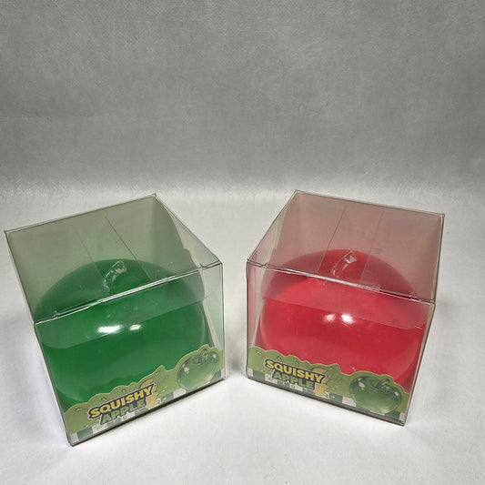 Two small clear plastic boxes containing round red and green apple, photographed on a light gray textured background.