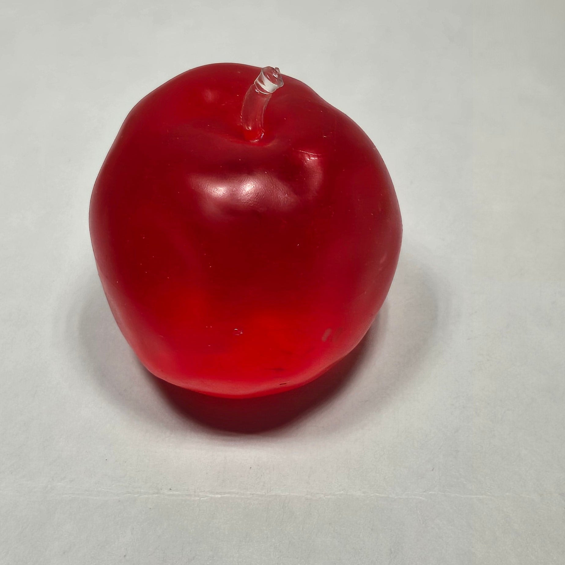 A single red, glossy, apple-shaped sensory sits on a plain light gray textured surface.