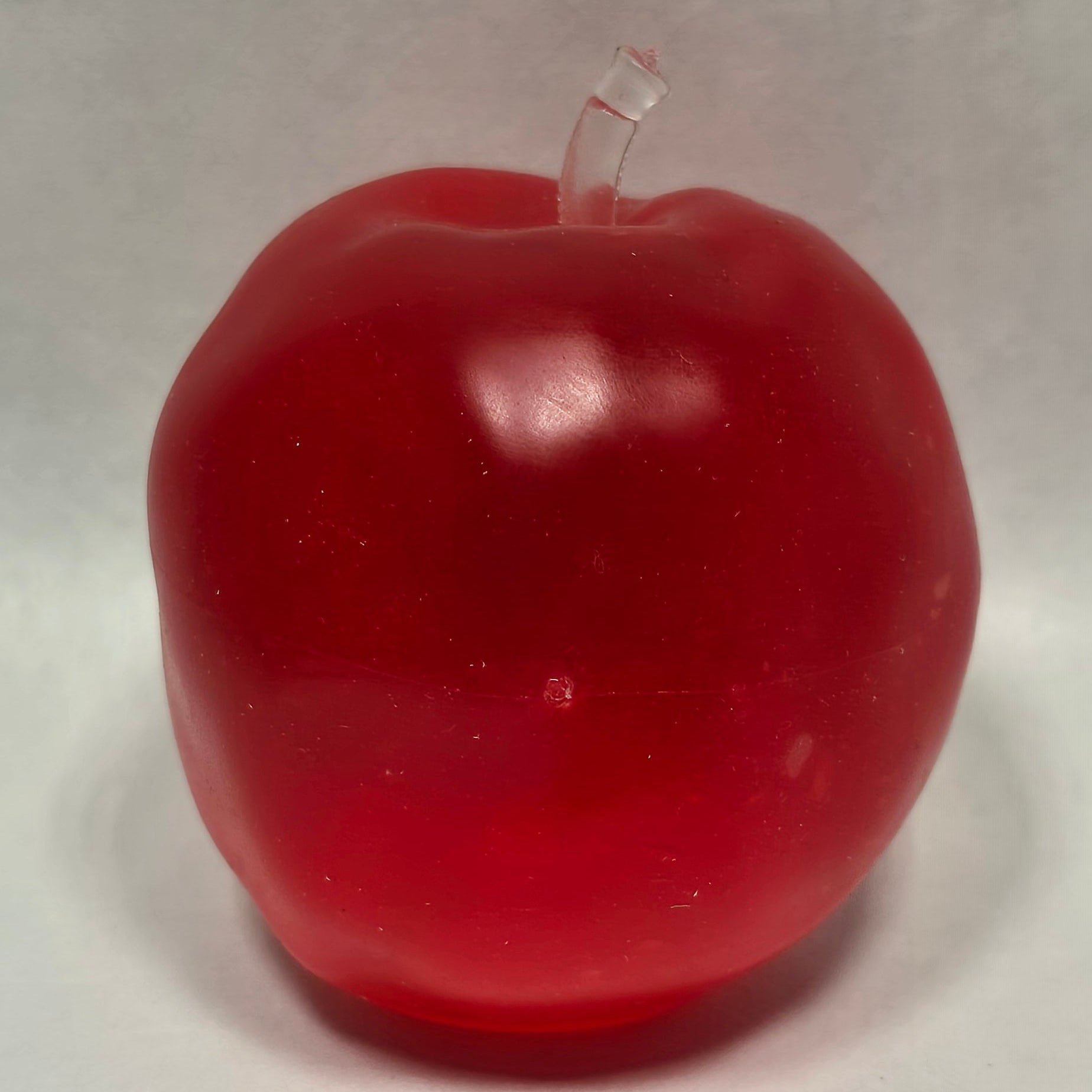 A red apple-shaped  sensory toy with a small clear stem, photographed on a plain light background.
