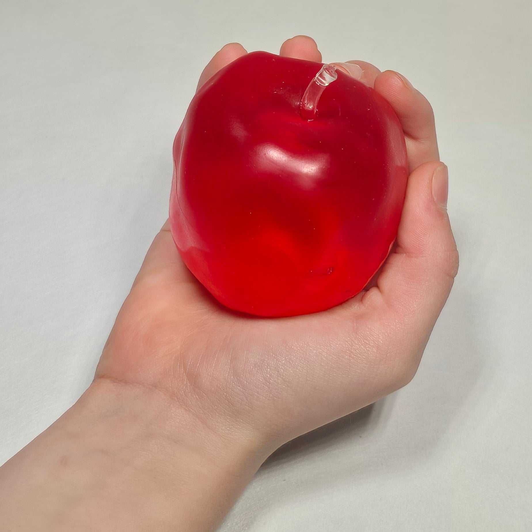 A hand holding a small, translucent red stress ball against a plain light gray background.