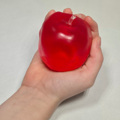 A hand holding a small, translucent red stress ball against a plain light gray background.