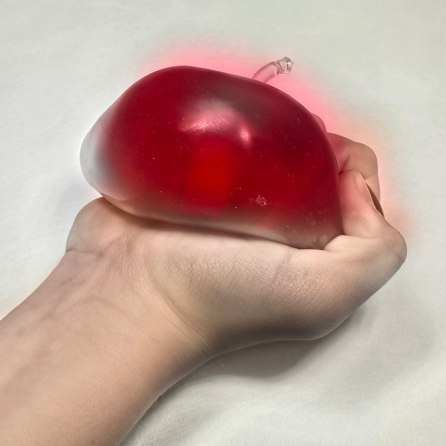 A hand squeezing a translucent red squishy toy against a plain light background.