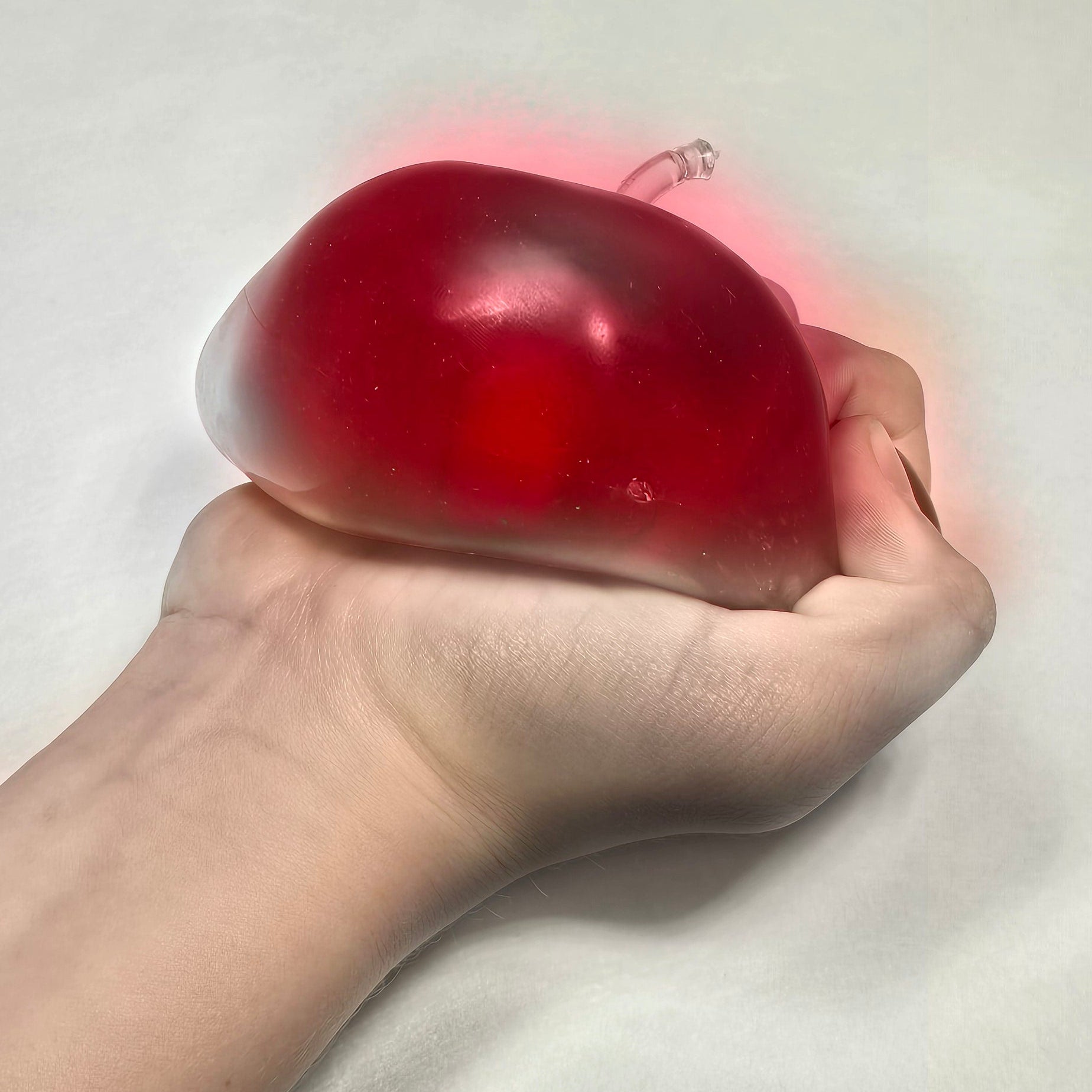 A hand squeezing a translucent red squishy toy against a plain light background.