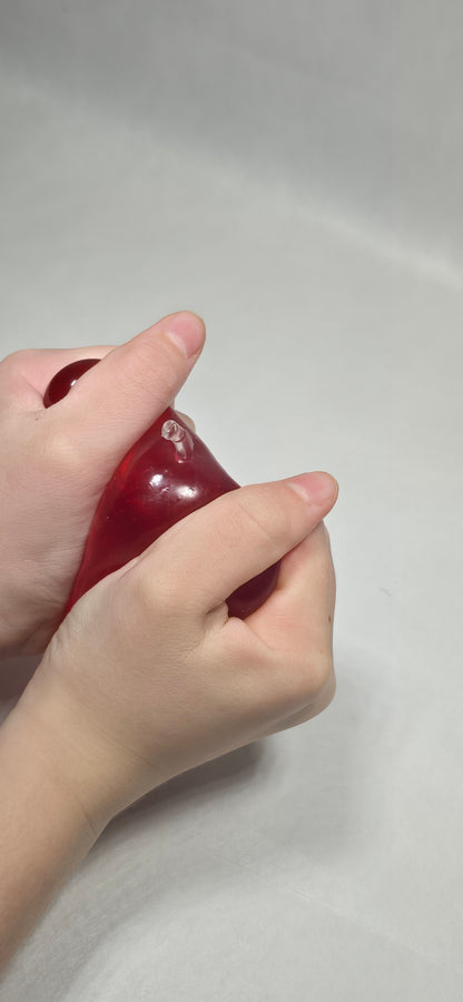 A close-up of a person's hands squeezing a glossy, translucent dark red silicone or rubber toy against a plain light gray background.