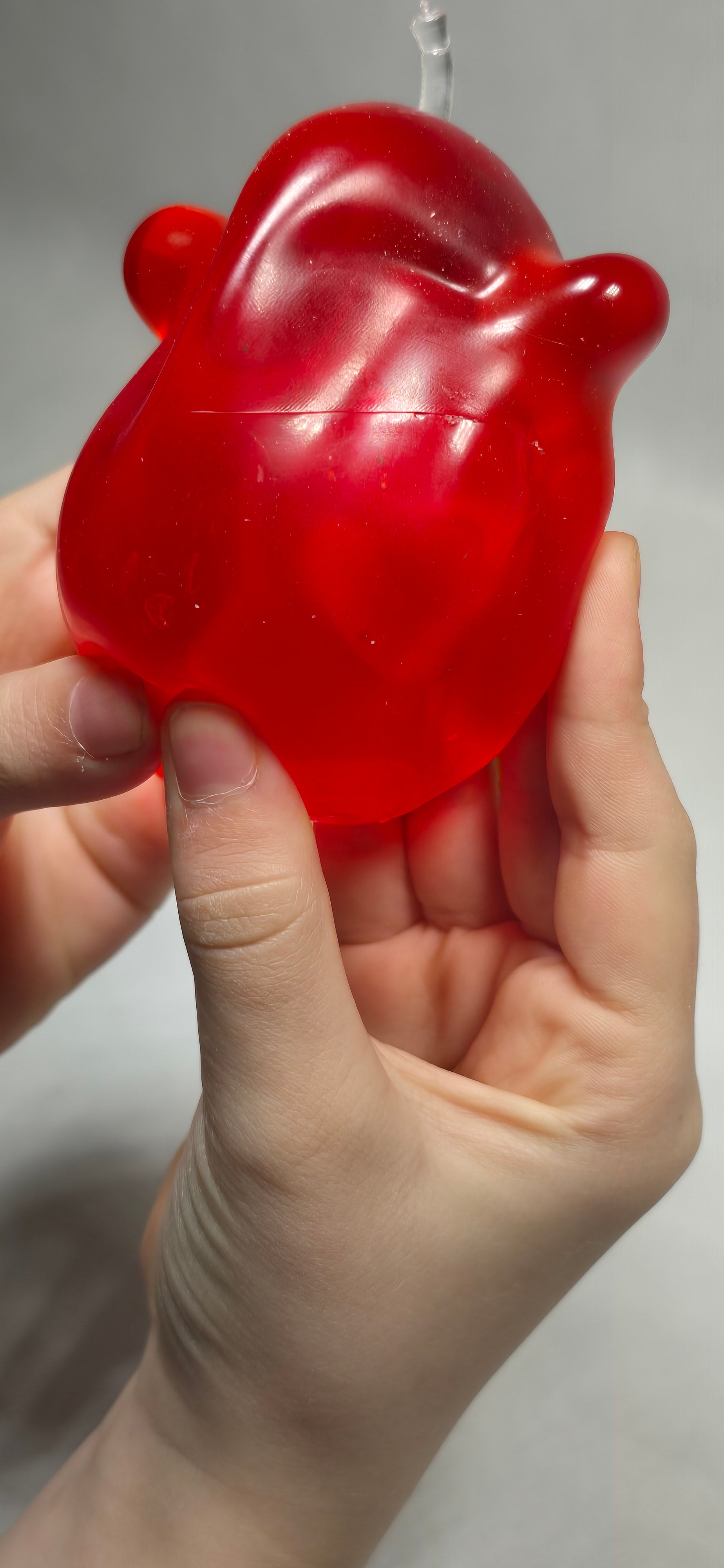 A hand holding a translucent red, apple shaped sensory toy against a plain light gray background.