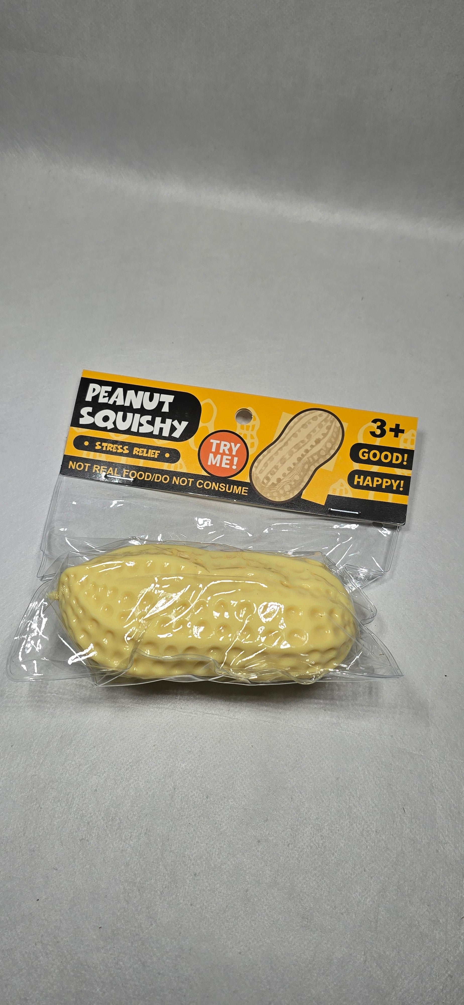 A packaged novelty peanut-shaped squishy toy on a light gray background. The toy is yellow and textured like a peanut, sealed in clear plastic packaging with a yellow and black backing card that reads 'PEANUT SQUISHY' 
