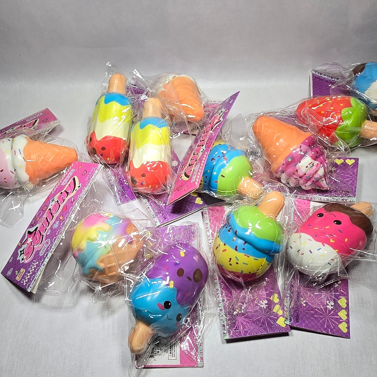 A group of small, colorful novelty squishy toys in clear plastic wrappers with purple backing cards, arranged on a light gray fabric background.