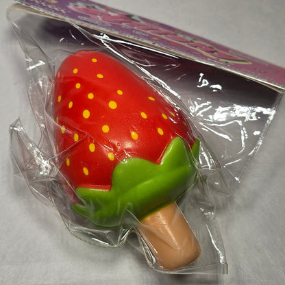 A small strawberry-shaped product wrapped in clear plastic with a purple backing card, photographed on a light gray surface.