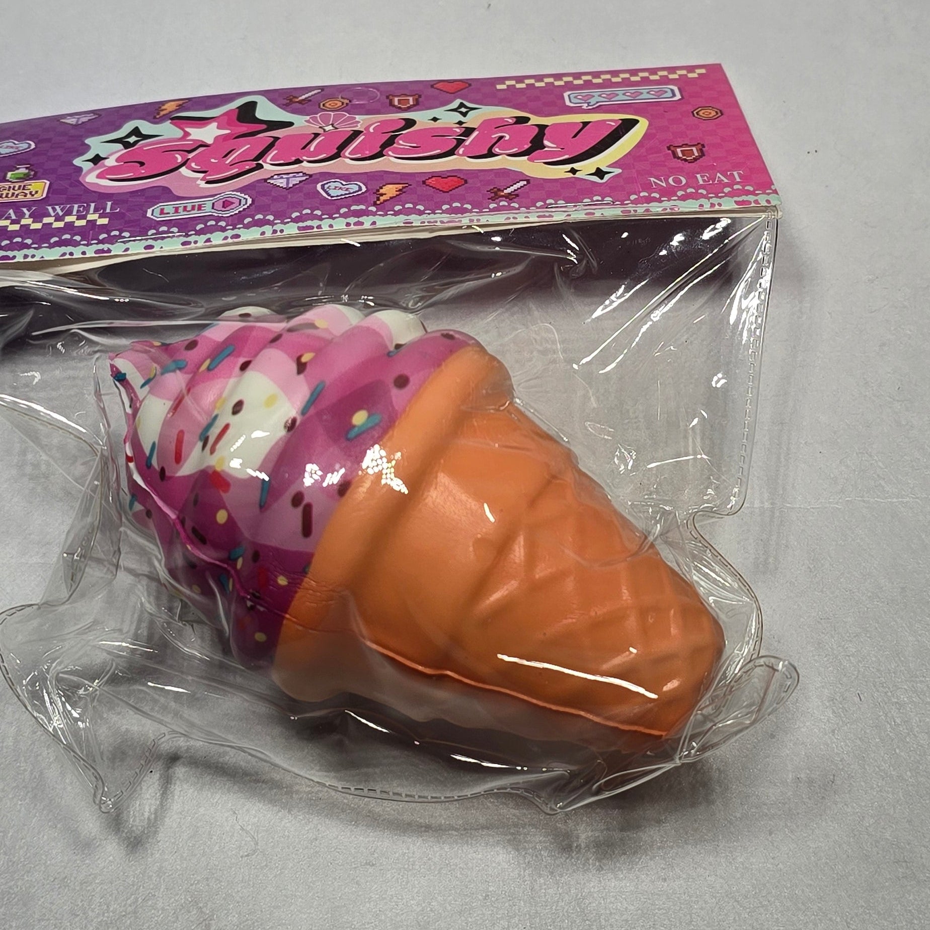 A small ice cream cone toy in its original pink and white blister packaging, photographed on a plain light gray background.