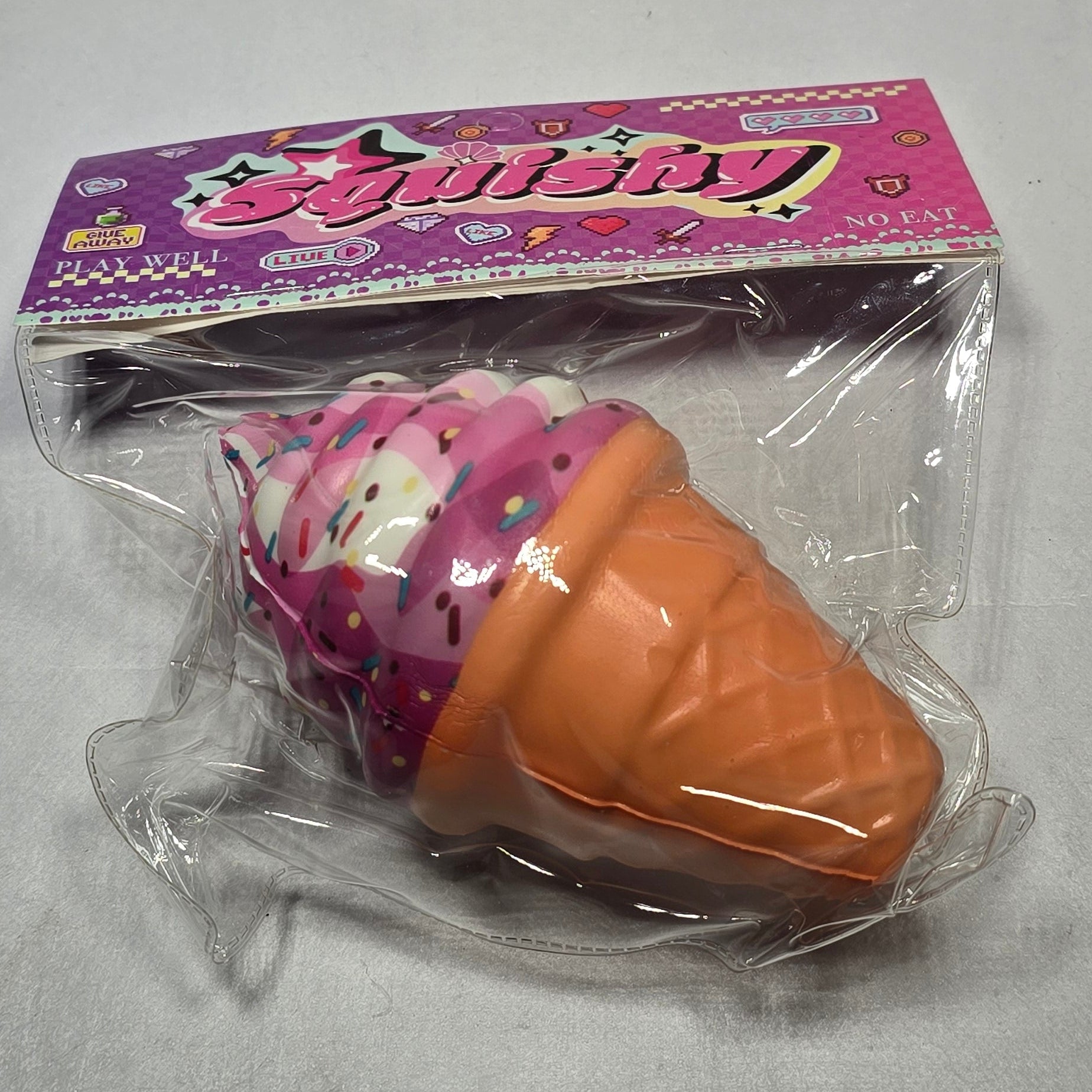 A packaged ice cream cone toy with a pink and white body and an orange cone, sealed in clear plastic with a purple branded card backing, set against a light gray background.