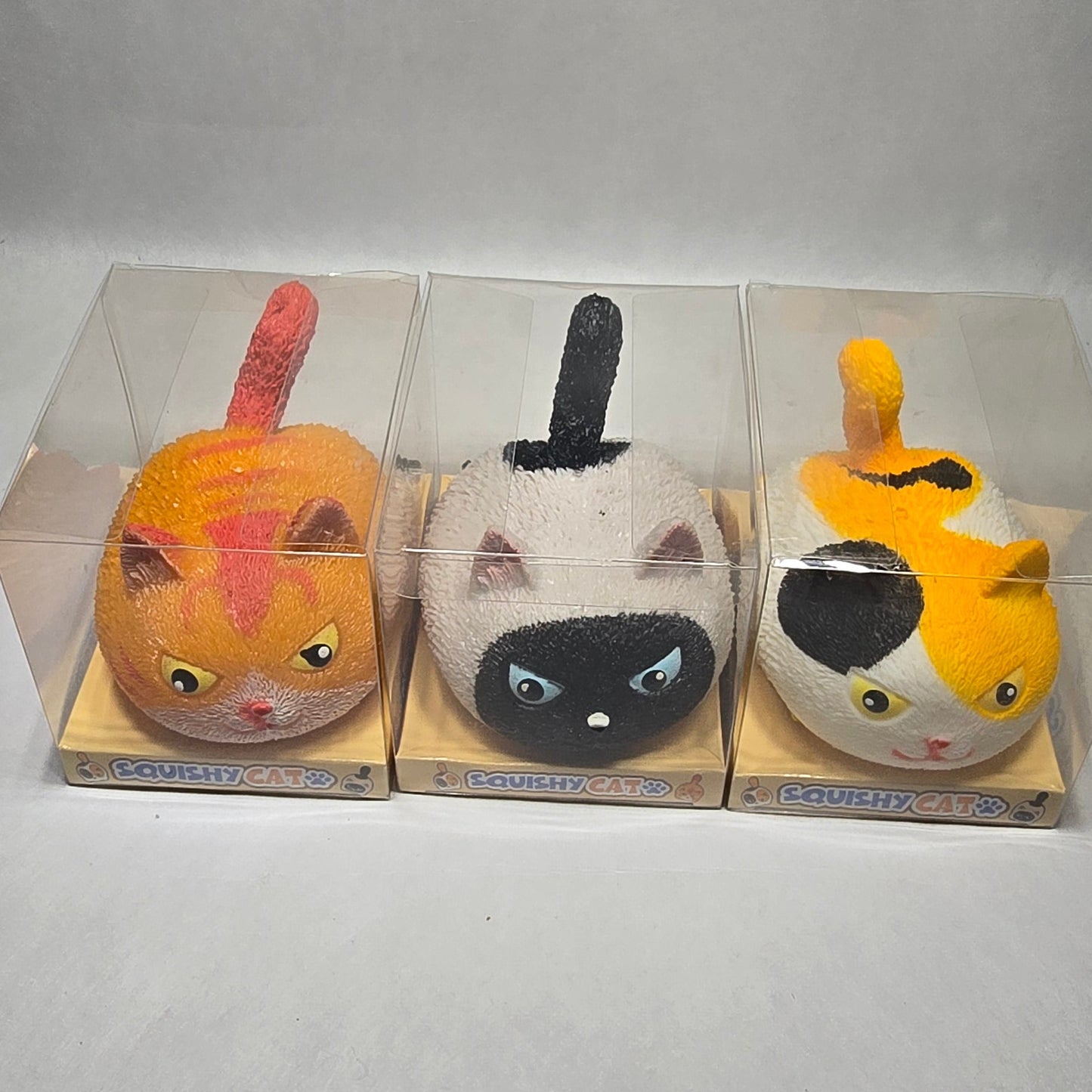 Three small squishy animal toys in clear plastic packaging, arranged vertically against a light gray textured background.