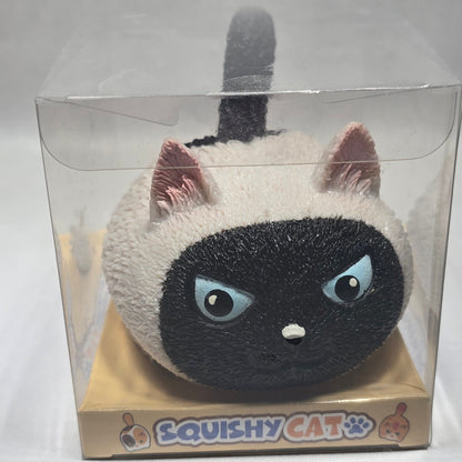 A squishy cat toy inside a clear plastic sleeve, featuring a black and white Siamese cat face with large blue eyes and pink ears, on a beige backing card labeled 'Squishy Cat'.