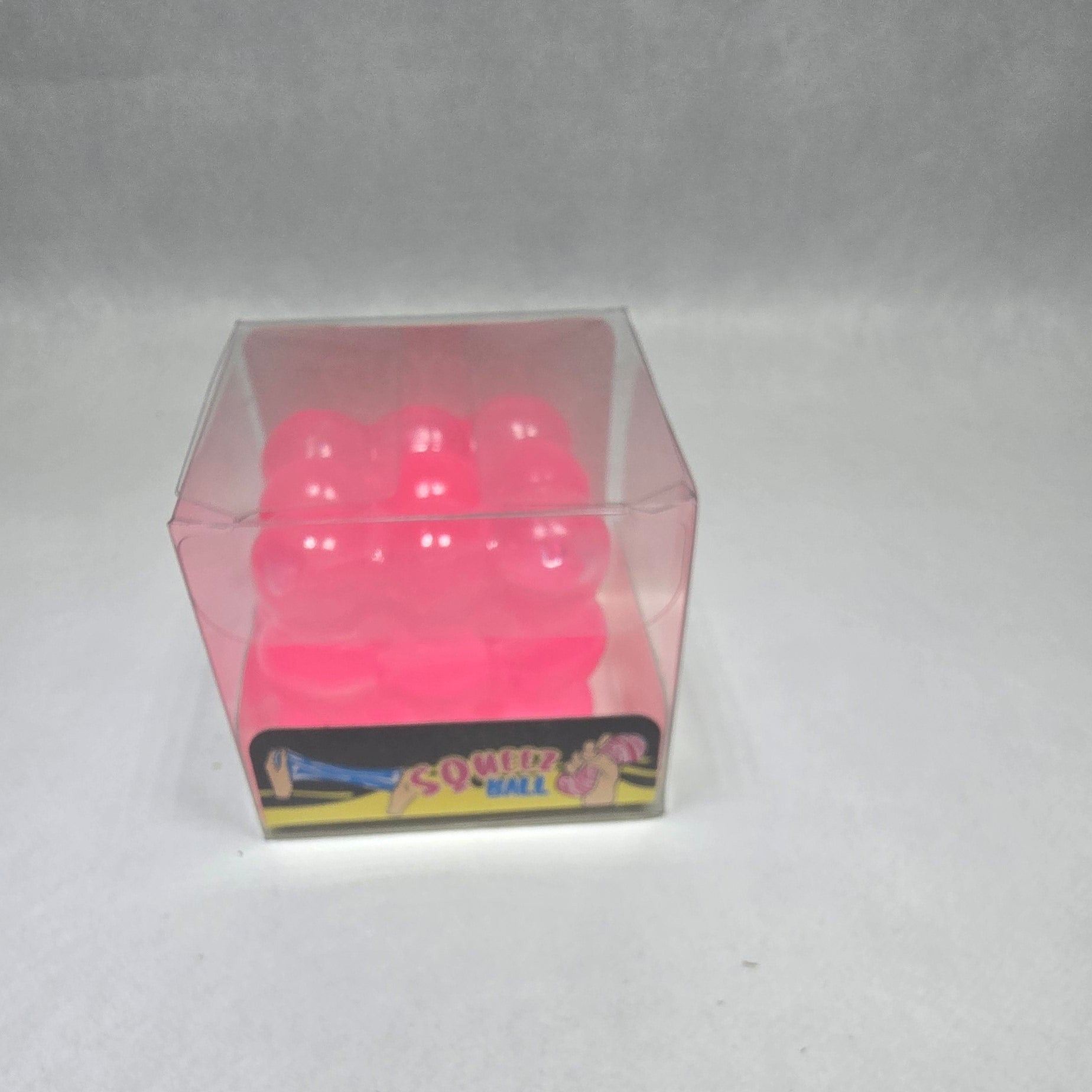 A small pink translucent cube-shaped item with white dots on a white textured background, next to a colorful rectangular card.
