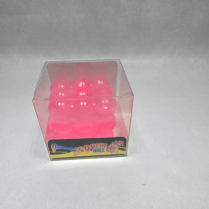 A small pink translucent cube-shaped item with white dots on a white textured background, next to a colorful rectangular card.