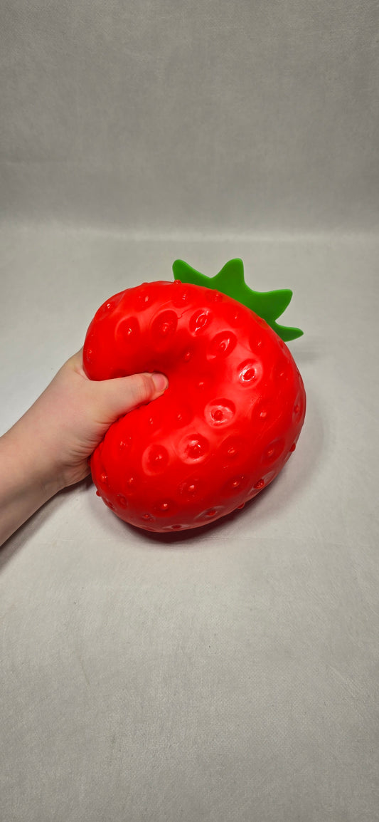 A hand holding a red strawberry-shaped squishy toy against a plain light gray background.