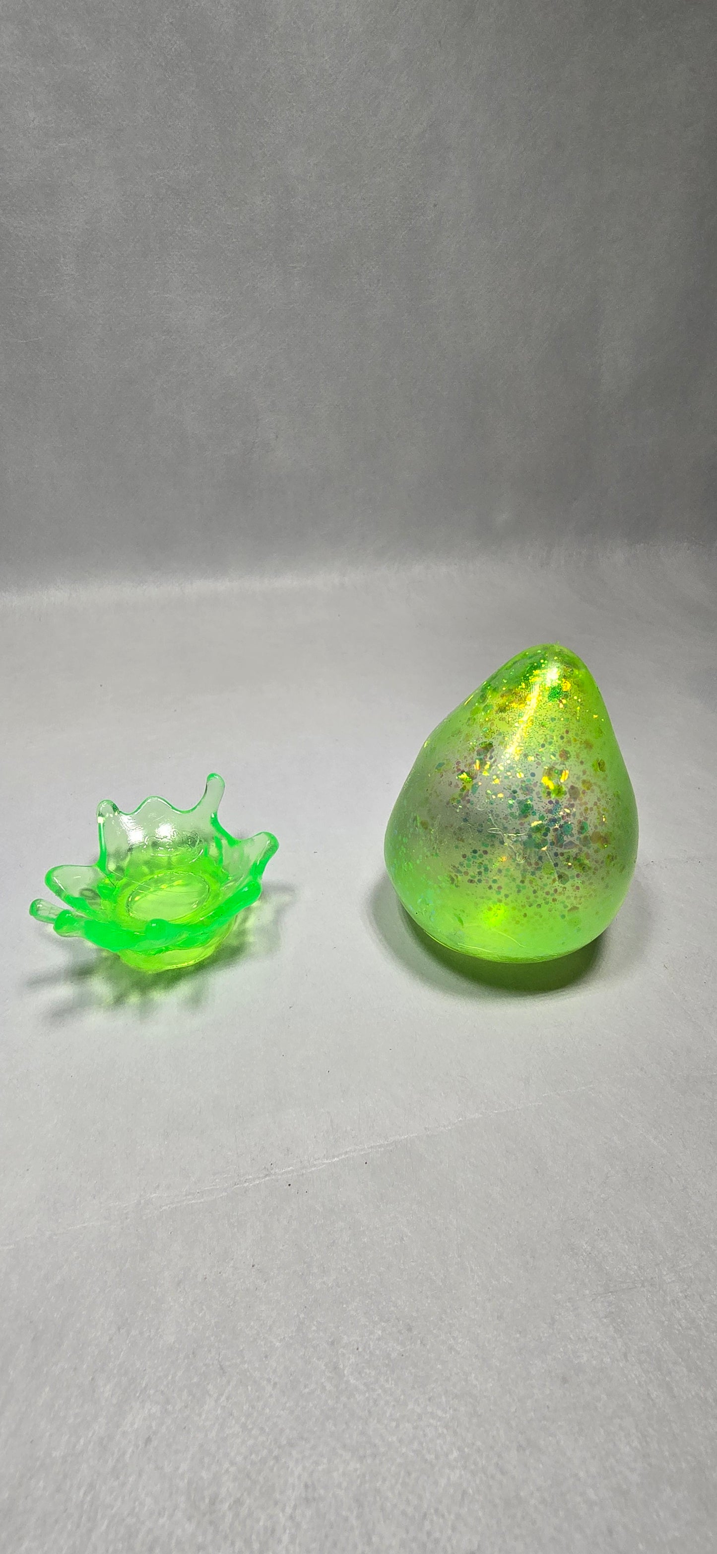 A translucent neon green silicone applicator sponge and a matching textured green sponge tip, displayed on a plain light gray surface.