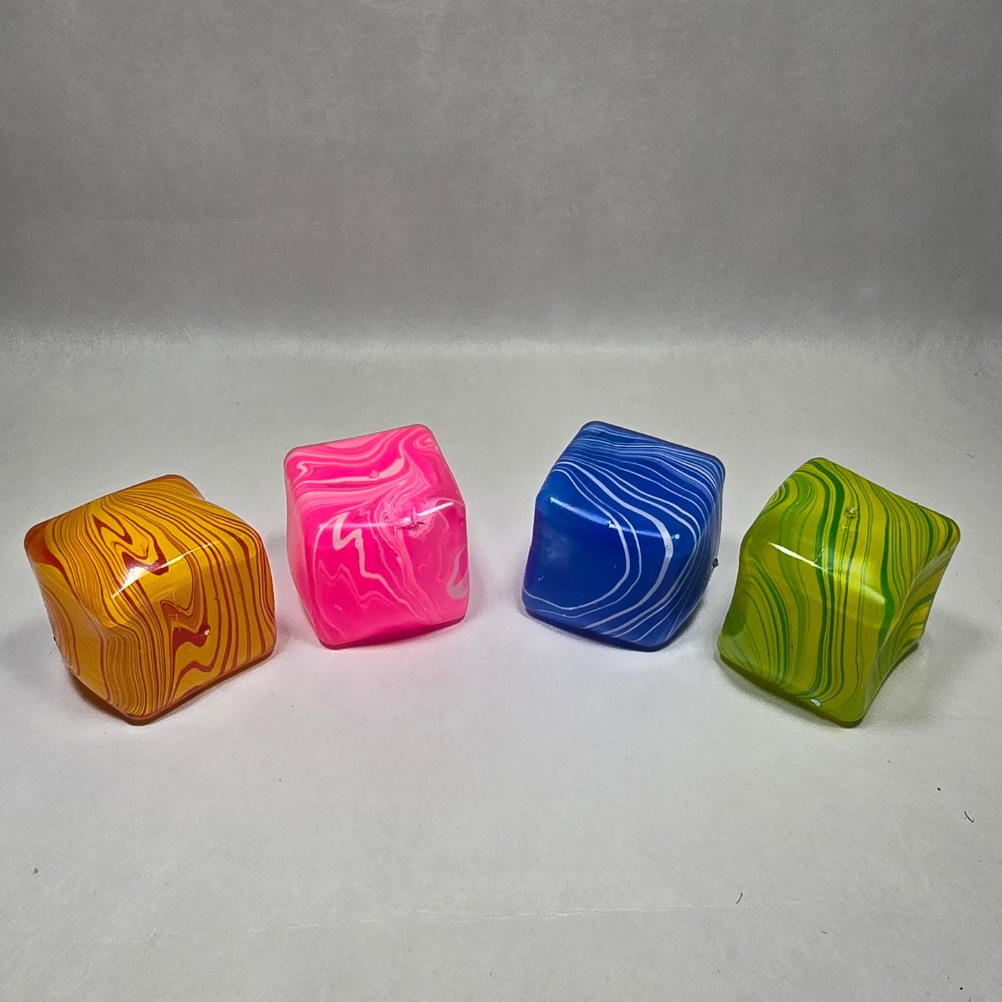 Four small, translucent, wavy-edged decorative beads or charms in lime green, royal blue, hot pink, and amber orange, arranged vertically on a light gray textured background.