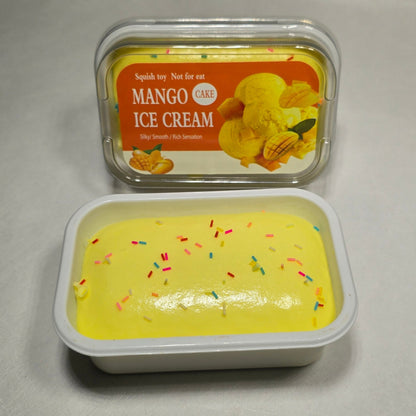 Two small plastic containers of mango ice cream on a light gray surface. One container is closed with a printed lid showing a mango illustration and the text 'MANGO ICE CREAM'.