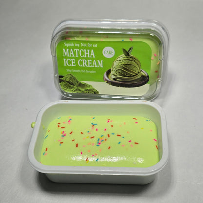 An open plastic container of matcha ice cream showing the pale green cream inside with colorful sprinkles, next to its green label on a gray surface.